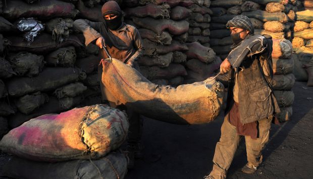 Trabajadores afganos llevan un saco de carbón triturado en un mercado de venta de carbón en las afueras de Kabul, Afganistán. (Foto referencial: EFE)